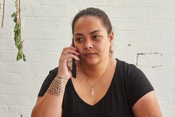 Image of an adult woman sitting at a desk, holding a mobile phone to her ear.