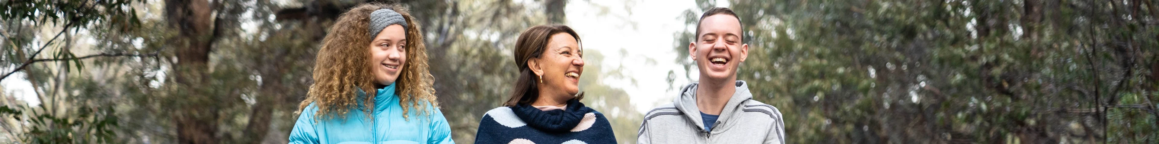 Image of a mother and two teens going on a bush walk. The teenage girl and the mother are laughing while looking left towards the teenage boy, who is laughing loudly.