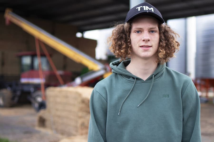 Ben boy wearing cap with hay stack and tractor behind him