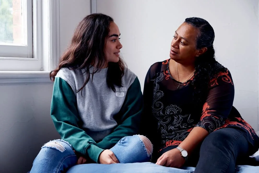 teen daughter and mother sitting by a window and looking supportively at each other