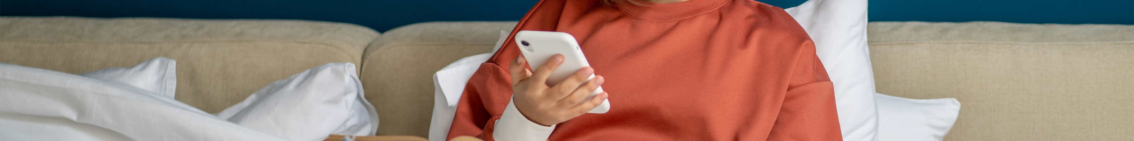 Image of a teen girl sitting in bed, holding her phone.