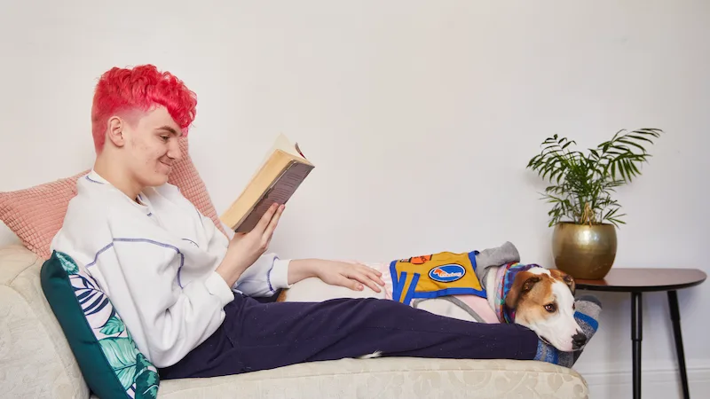 Teenager reading on couch with dog PC