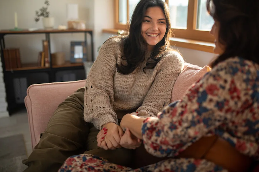 Young woman on couch holding hands with mother