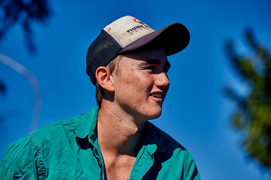 Young man wearing cap and collared shirt looking away from camera with trees in background