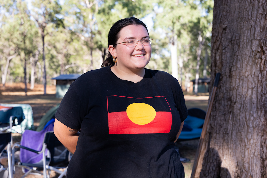 Image of Phoebe McIlwraith smiling and looking off camera. She is wearing a shirt that features the Aboriginal flag.