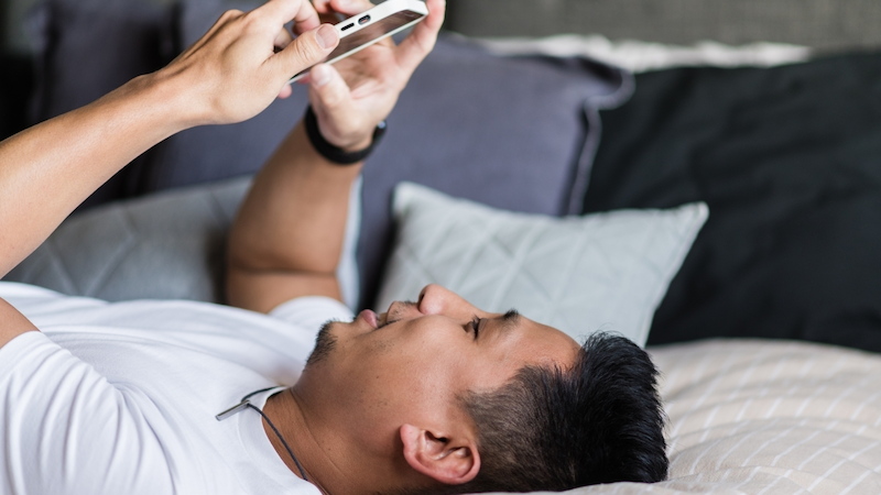 young man lying down on bed scrolling phone PC