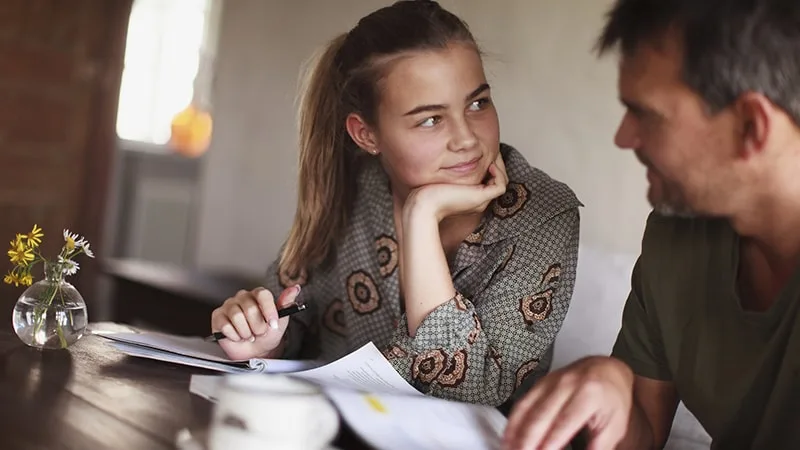 girl sitting at table with father talking books open in front of her