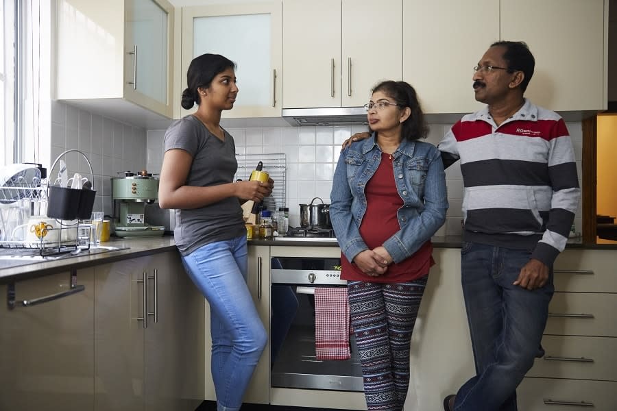 Girl with yellow cup talking to parents in kitchen