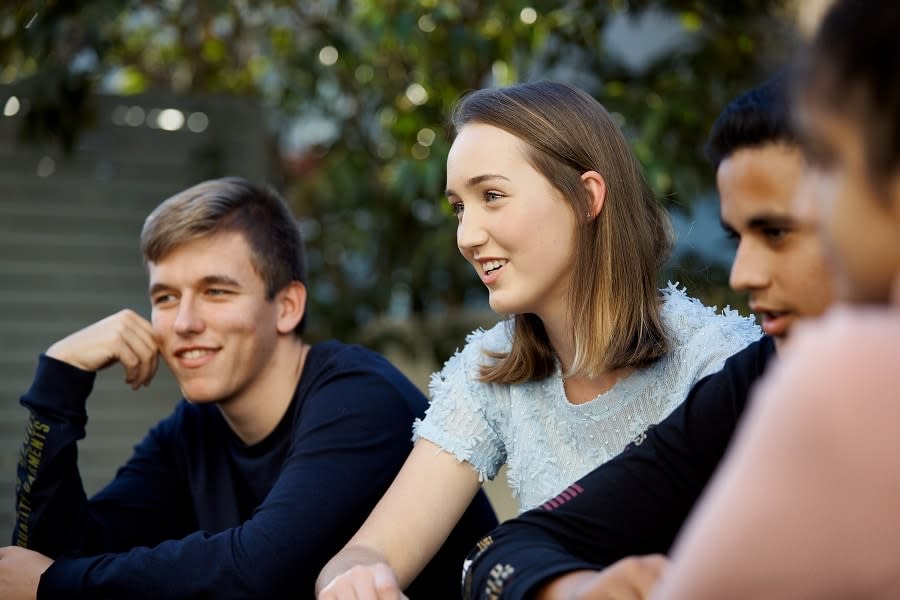 three young people sitting outside smiling