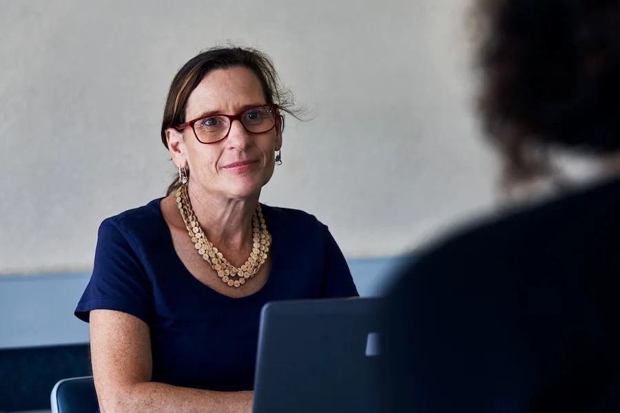 Image of an adult woman looking across a desk at a young person with a slight smile.