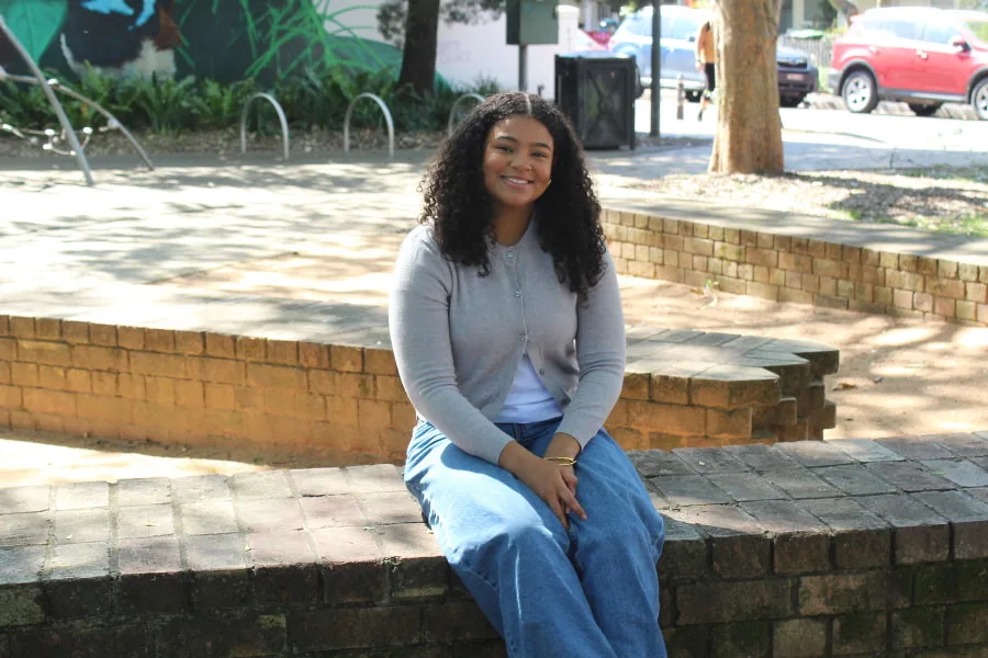 Anisha Damaso sitting outside on a park wall smiling at camera