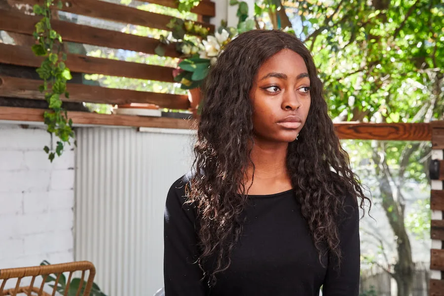 Image of a teen girl sitting outside. She is looking into the distance and wears a neutral expression.