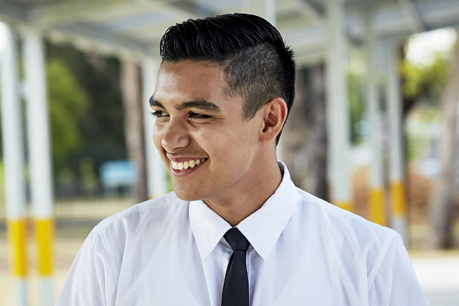 Image of a young boy at high school in his uniform. He is looking away from the camera and smiling.