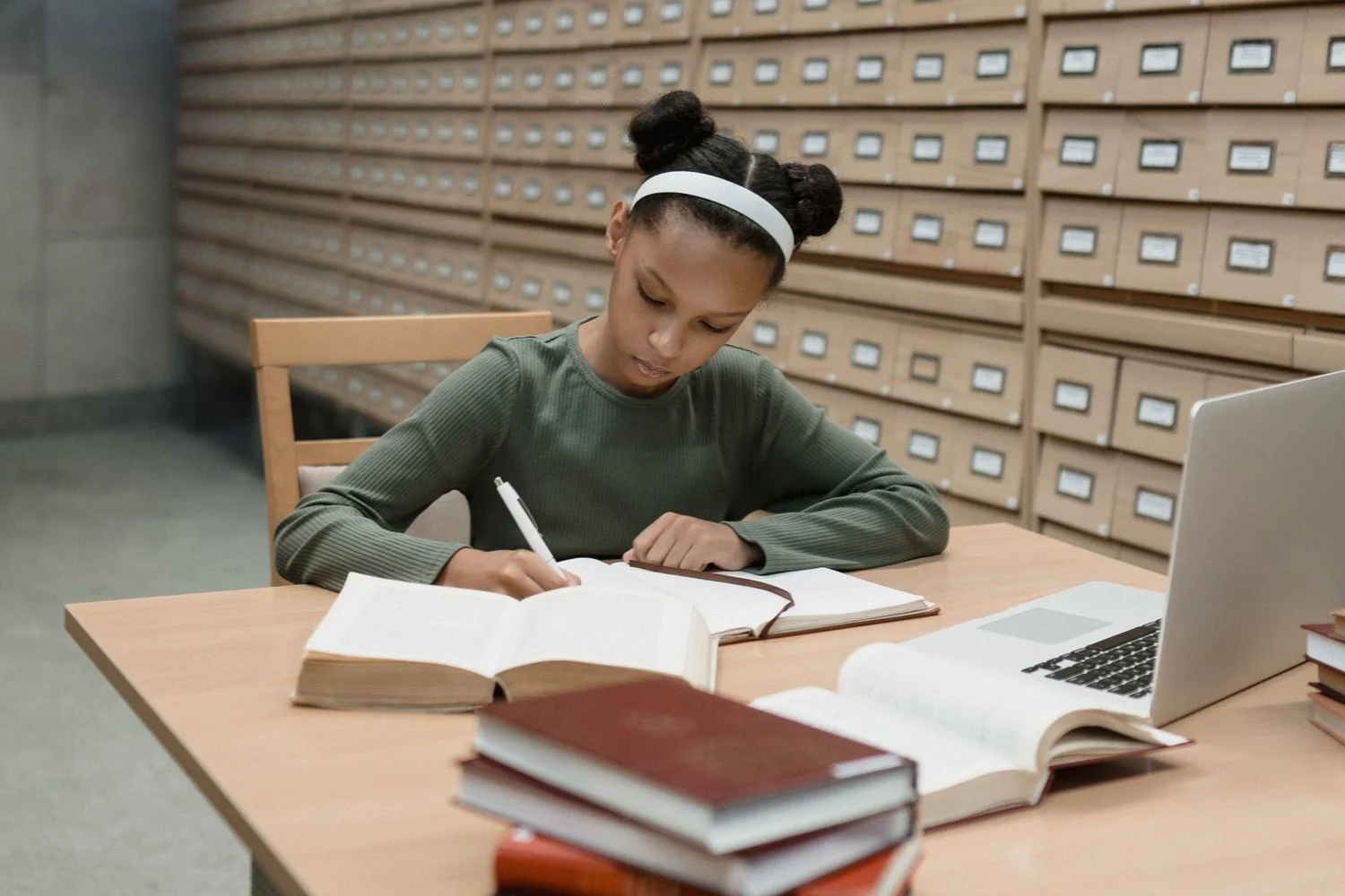 Young girl studying at desk with laptop and books