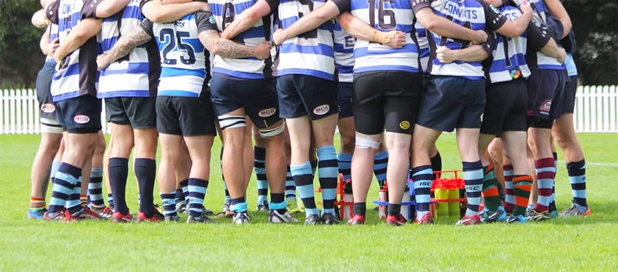 back view of rugby team huddled in a circle with arms around each other