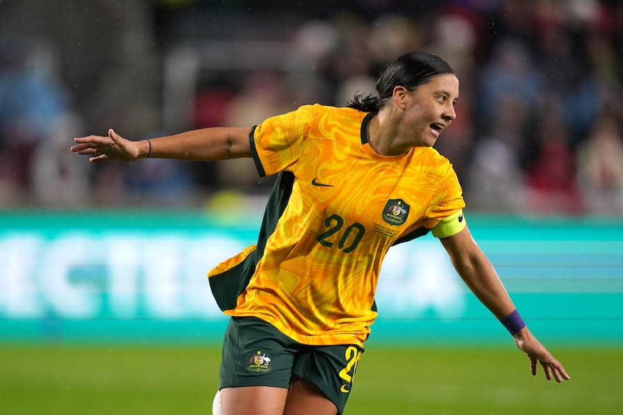 Image of Sam Kerr celebrating a goal on a football pitch, with her arms extended out wide and a big smile on her face. 