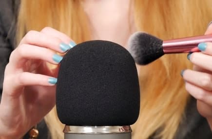Image of a woman running a brush over a microphone.