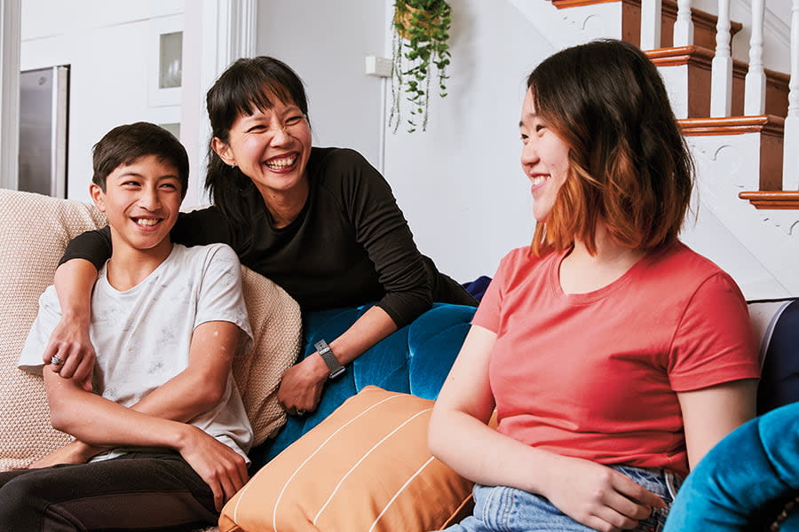 Image of a mother and her two teens laughing together in their lounge room.