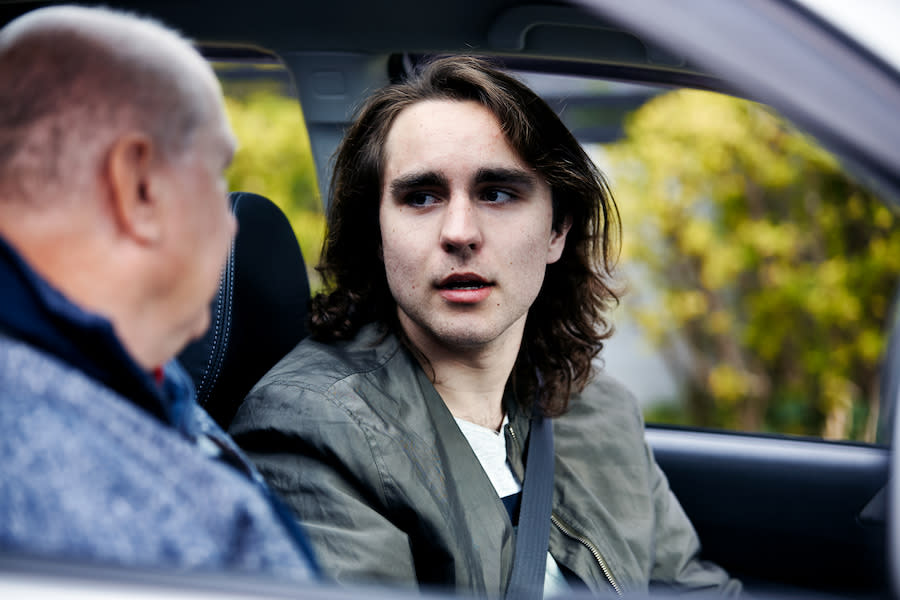 Image of a teen boy having a tense conversation with his dad in their car.