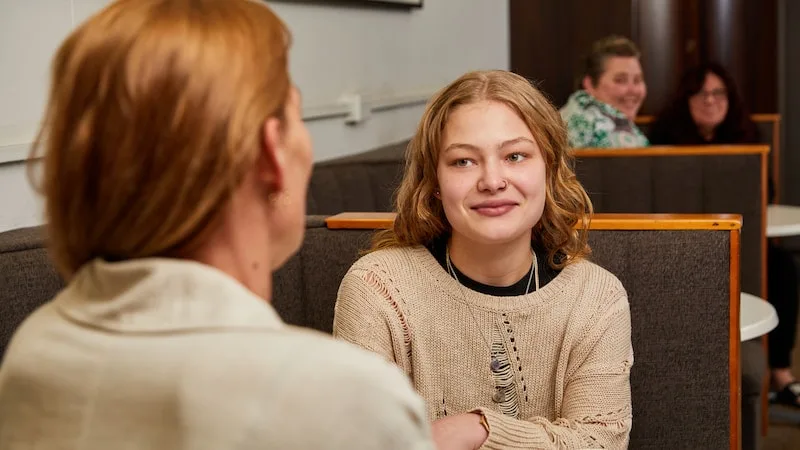 a young person talking to their parent in a cafe