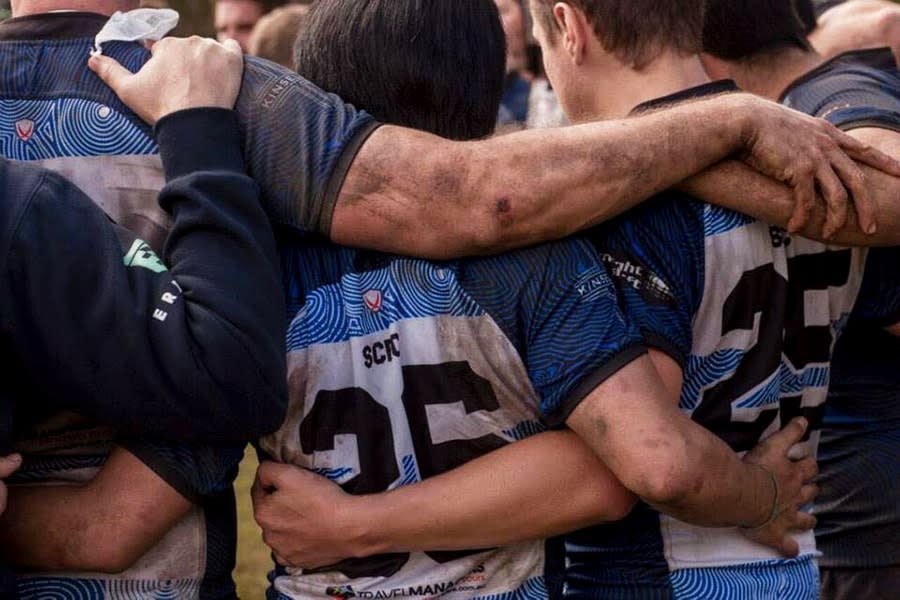 back view of rugby teammates huddled in a circle with arms around each other