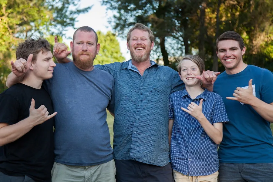 Image of a family with two male adults and three male children with their arms around each other, looking happy and smiling.