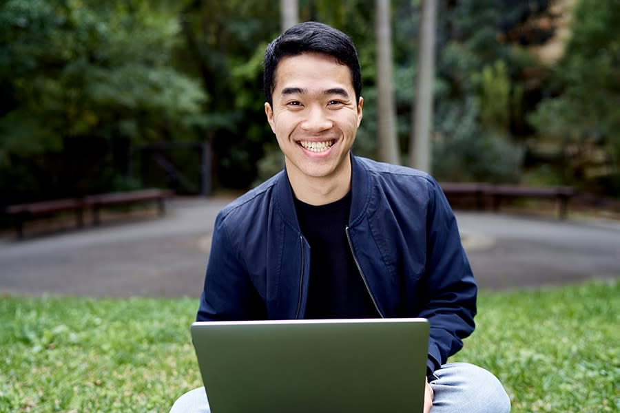Kwan guy smiling holding laptop sitting on grass