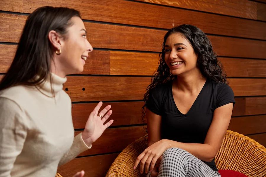 Image of two young women sitting together. Both are smiling and laughing.