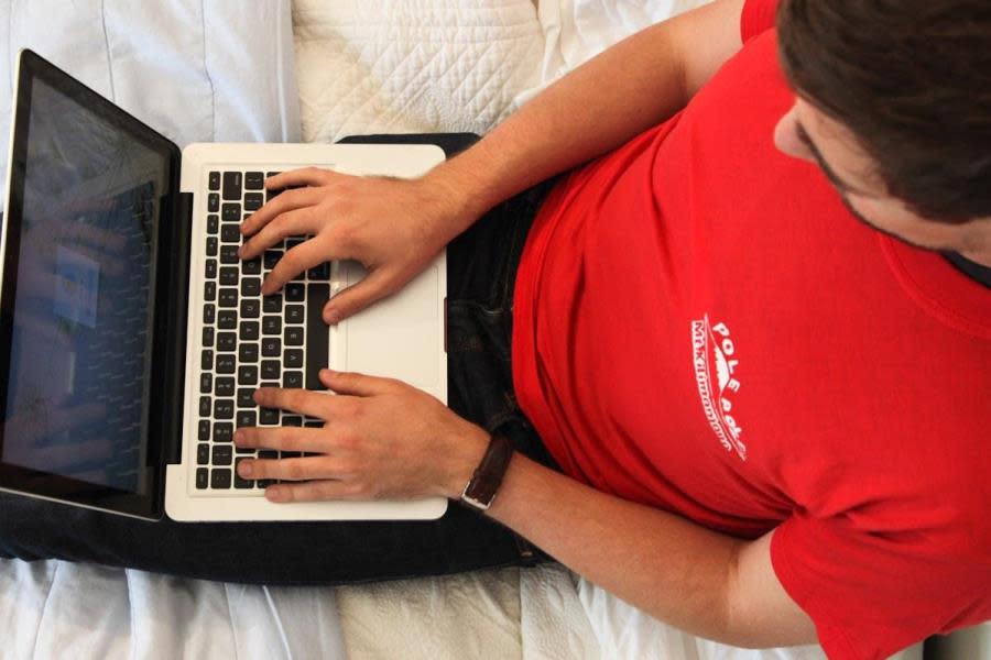Aerial view of guy typing on Mac computer on bed