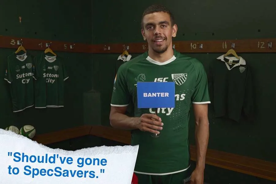 young man wearing green rugby uniform in locker room holding sign that says banter