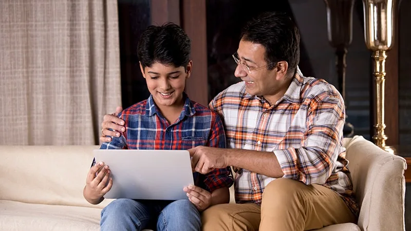 father and son sitting on couch looking at laptop