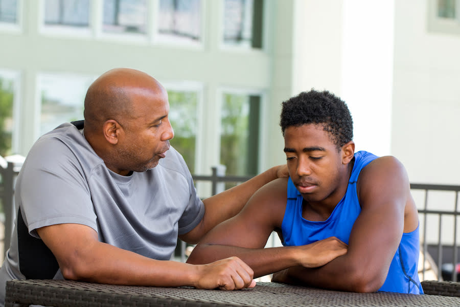 Image of a father comforting his teenage son at a table.