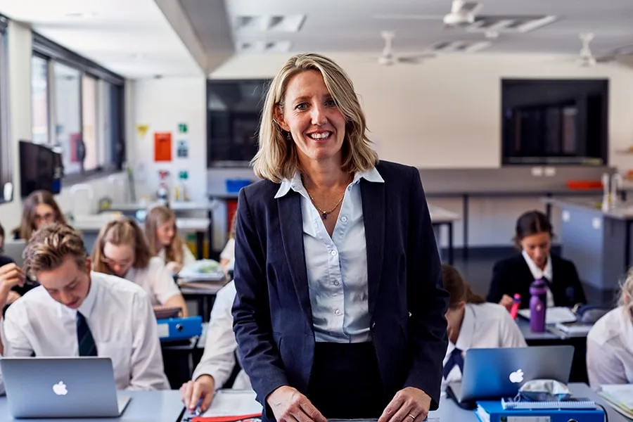 teacher smiling standing in front of classroom students at their desks