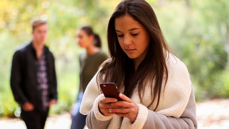 a girl on her phone in the foreground with two people in the background blurred