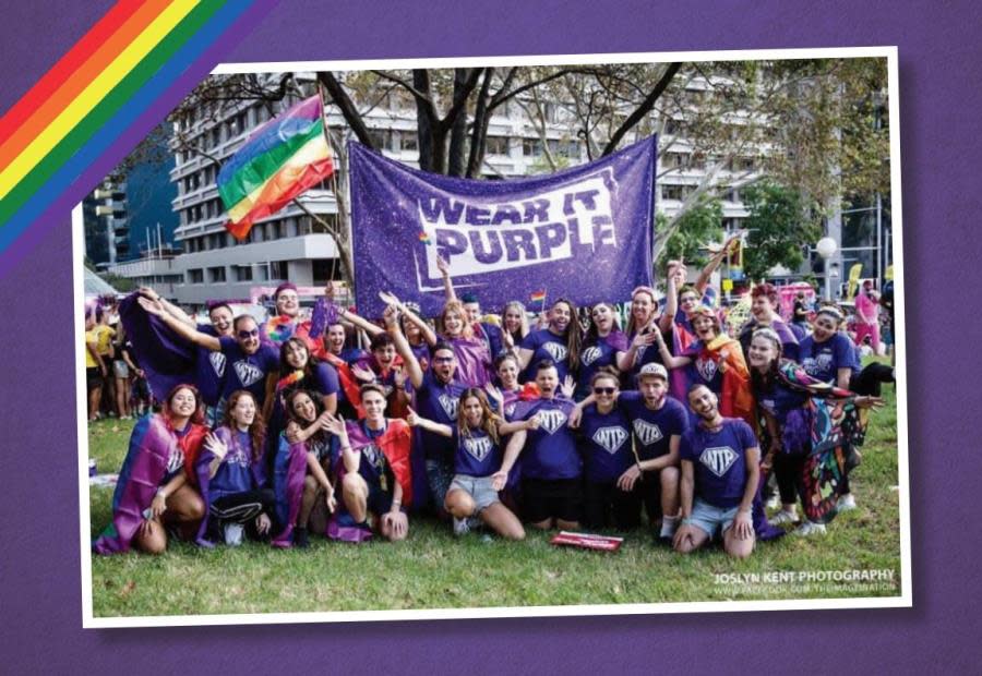 group of young people wearing purple shirts with a wear it purple banner and rainbow flag flying beh