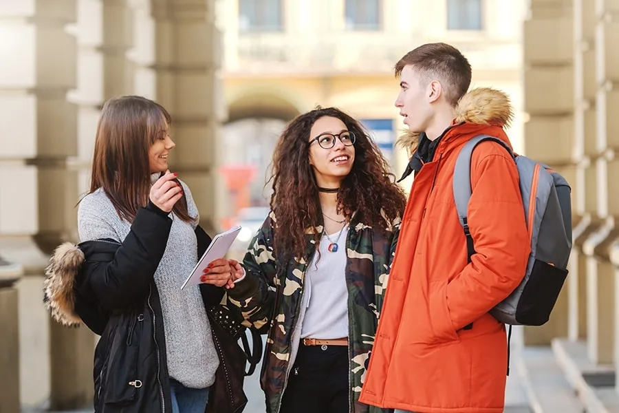 two girls and one guy talking to each other in courtyard