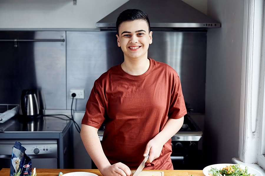 young guy smiling and chopping vegetables in kitchen