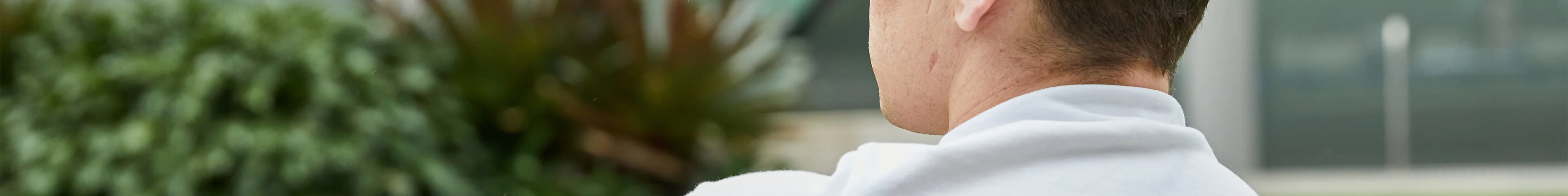 Image of a teen boy sitting outside. His back is to the camera and he's looking off into the distance.