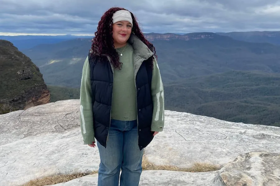 Image of Isabelle standing on a top of a mountain and smiling at the camera.