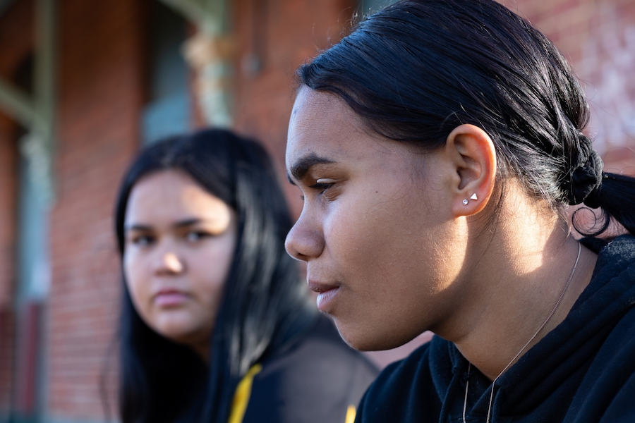 Image of two young brown-skinned First Nations girls, looking away from the camera.