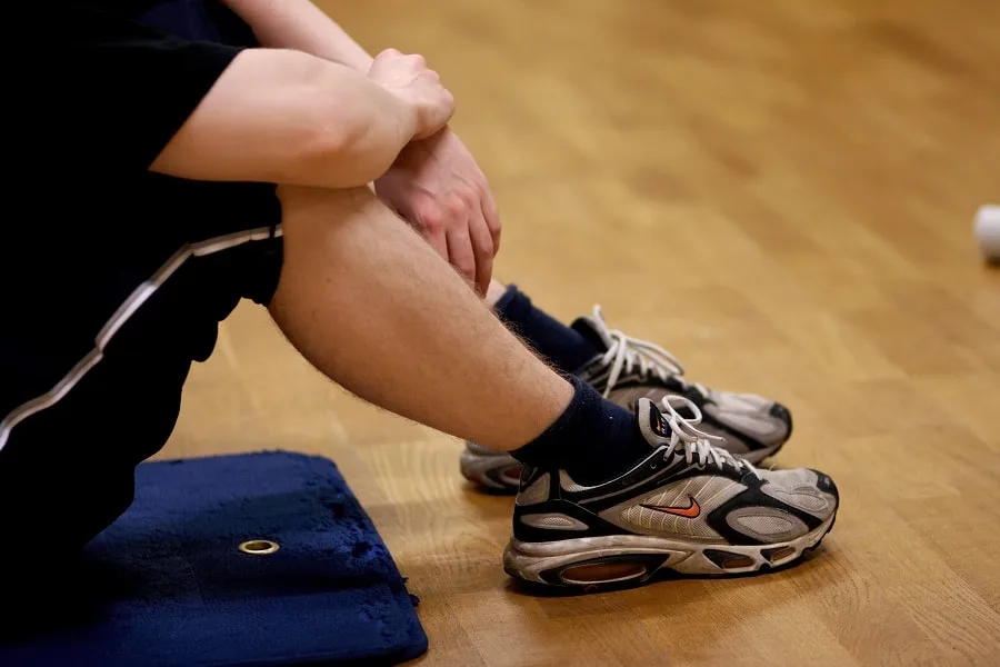 Boy sitting on blue mat with sneakers holding arm