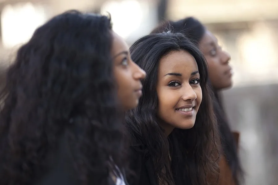 side view of three girls sitting in a row middle girl smiling looking at camera