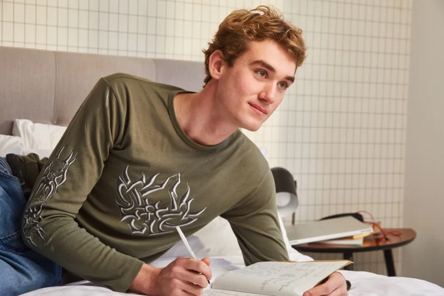 young person lying on their bed writing in a notebook