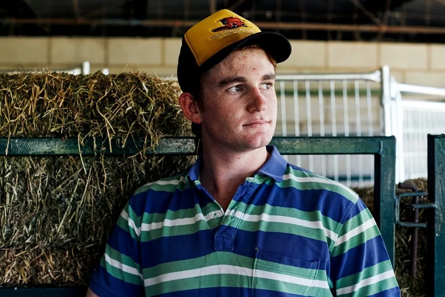 boy wearing hat next to hay