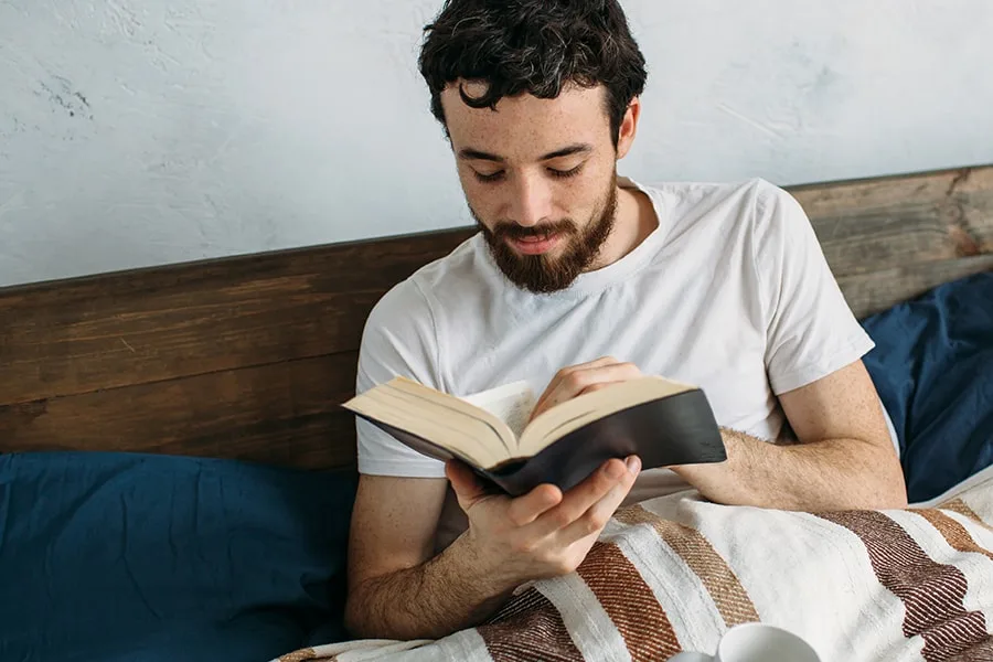 guy reading in bed with a mug feature