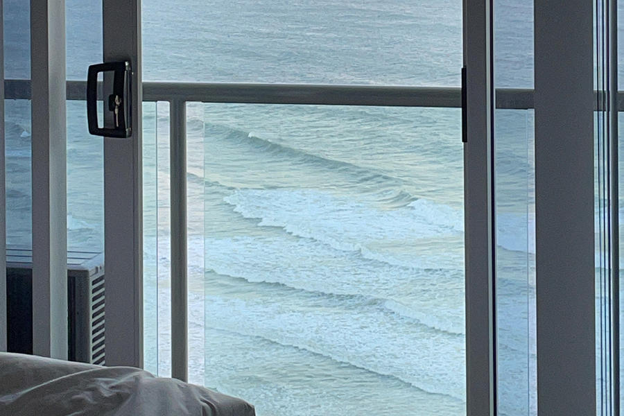 Image of the view from a bedroom balcony. The view is of ocean waves at dusk. 
