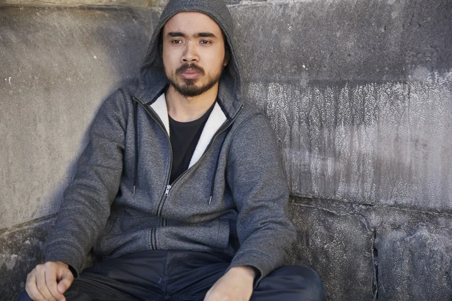 Young man with grey hoodie on sitting against wall