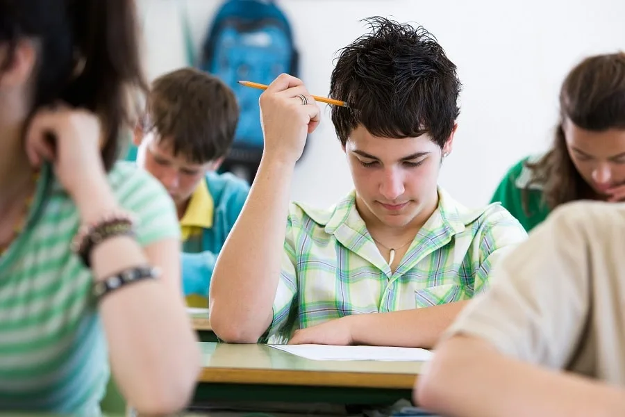 Boy in class with pencil looking down