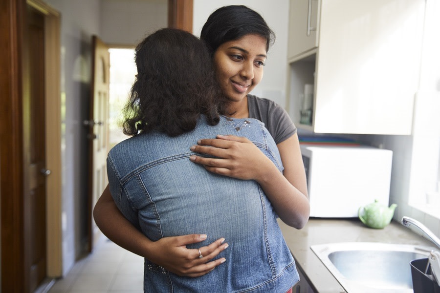 Girl in denim jacket hugging friend in kitchen