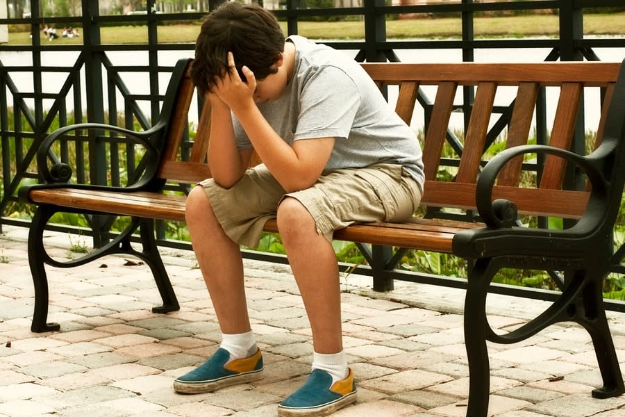 Boy with head in hands sitting on bench